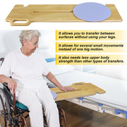 Older woman seated in a wheelchair beside a bed, with a wooden transfer board bridging the two surfaces and a blue rotating seat disc positioned near the wheelchair.