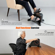 Dual-function pedal exerciser shown with a seated user pedaling for leg exercise and a senior using hand grips for arm exercise at a table.